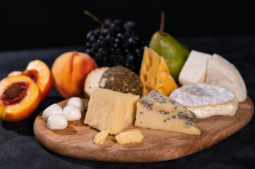 Various kinds of cheese with walnuts and grapes. Wine plate. Close-up, dark background.