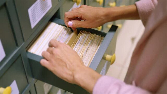 A woman hand searching cards in old wooden card catalogue. A vintage library catalogue, for a convenient and quick search for a book. Search for information in the card file in the library.