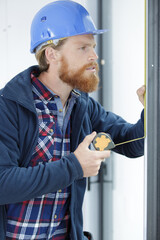 bearded workman measures frame of glass door