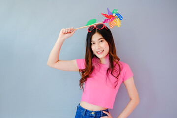 Obraz na płótnie Canvas Portrait beautiful asian teen girl wearing pink dress on gray background, fashion summer set with colorful wind turbine or pinwheel or wind toy holding in hand, emotions action, happy life concept