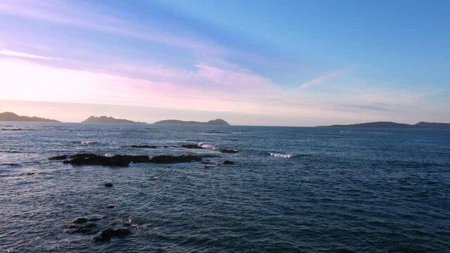 Aerial view of sea waves breaking over rocks in O Vao beach on spectacular sunset in Vigo, Pontevedra, Spain. Dolly forward near ground.