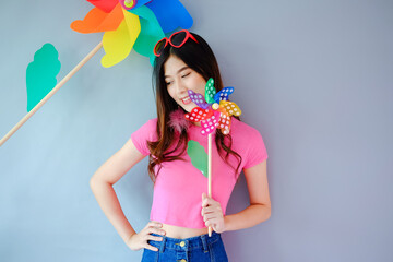 Portrait beautiful asian teen girl wearing pink dress on gray background, fashion summer set with colorful wind turbine or pinwheel or wind toy holding in hand,  emotions action, happy life concept