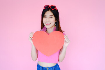Portrait beautiful asian woman on pink background, happy valentine day in love concept, model holding red heart sign in hand