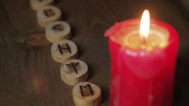 Burning candle on a wooden table with a row of runes
