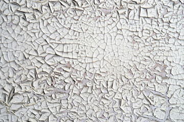 White peeling paint on the wall. Weathered rough painted surface with patterns of cracks