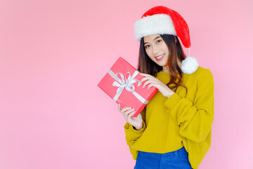 posing asia woman wearing long sleeve clothes on pink background with Santa Claus hat and red gift box holding in hand, holiday in festive Christmas or X'mas and happy new year concept, Winter fashion