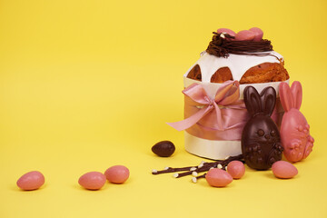 Beautiful Easter composition with Easter cake, chocolate eggs and a hare on a colored background, space for text.
