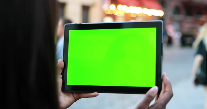 Female Hands Holding Tablet With Green Screen. Girl Using Mobile Phone While Walking In The Autumn Street. Back View Shot. Chroma Key, Close Up Woman Hand Holding Device With Vertical Green Screen