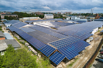 Aerial view of blue photovoltaic solar panels mounted on industrial building roof for producing green ecological electricity. Production of sustainable energy concept.