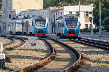 Two local diesel trains of two carriages in blue paint on the platform of a small town station.