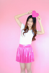 Portrait beautiful asian teen girl wearing white T-shirt and pink skirt on pink background, happy valentine day in love concept, model holding red heart sign in hand