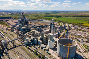 Fototapeta premium Aerial view of cement plant with high concrete factory structure and tower crane at industrial production area. Manufacture and global industry concept.