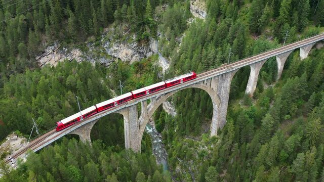 Dramatic aerial drone footage of a train crossing the famous Wiesen viaduct bridge near Davos in Canton Graubunden in the alps in Switzerland. 