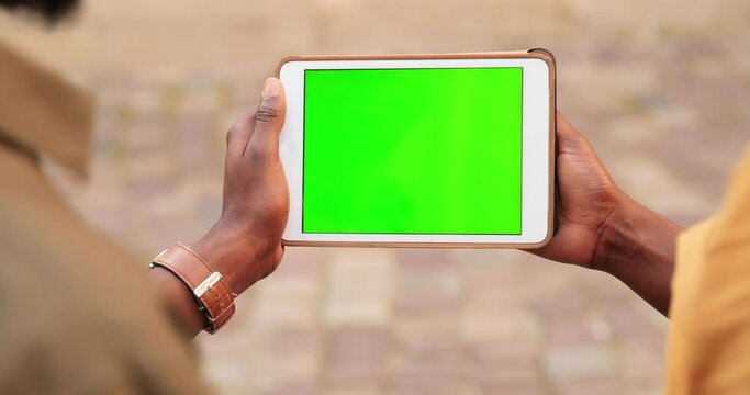 Rear of multiracial male and female friends looking at tablet with chroma key standing at the street and speaking. Colleagues looking at device with green screen. Close up