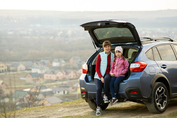 Side view of mother with daughter sitting in car trunk and looking on nature. Concept of resting with family on fresh air.