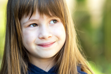 Portrait of pretty child girl with gray eyes and long fair hair outdoors on blurred green bright background. Cute female kid on warm summer day outside.