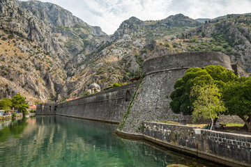 Fototapeta premium Kampana tower and medieval fortress walls with mountains and Scurda river green waters in the foreground, Kotor Bay, Montenegro