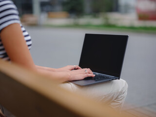 Young asian female student working at laptop sit down on bench outside on urban city street. Happy lady distance learning, education and online shopping. hands closeup