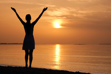 Fototapeta premium Lonely young woman standing on ocean beach by seaside enjoying warm tropical evening.