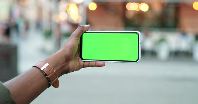 Rear of multiracial male looking at the smartphone with chroma key while standing at the street. Guy looking at device with green screen. Close up