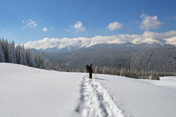 Man backpacker hiking snowy mountain hillside on cold winter day.
