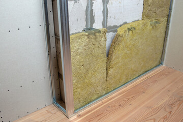 Wall of a room under renovation with mineral rock wool insulation and metal frame prepared for drywall plates.