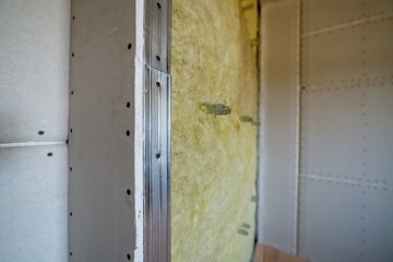Wall of a room under renovation with mineral rock wool insulation and metal frame prepared for drywall plates.