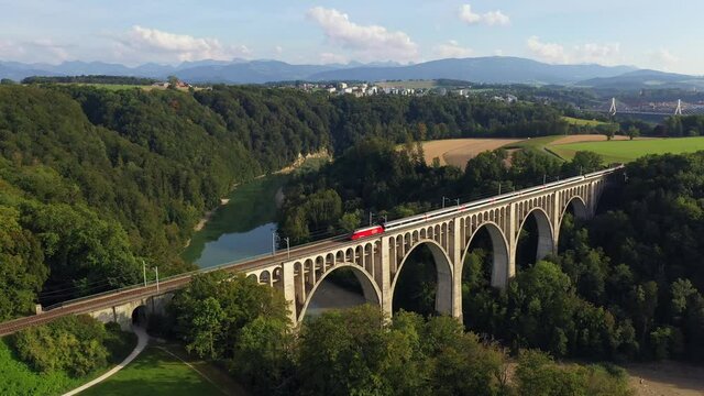 Aerial drone footage of a train crossing the famous Granfey viaduc, or bridge, over the Sarine river in Fribourg, Switzerland