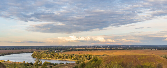 Colorful landscape in the evening, gorgeous blue sky with golden clouds over a field with hills and a river. A magical moment of nature.