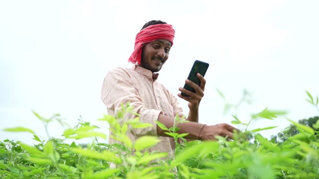 Young indian farmer using smartphone at agriculture field.
