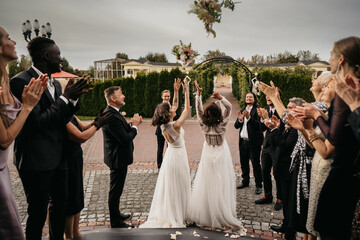 Candid shot of two female lesbian LGBT brides toss their bouquets over their shoulders to their...