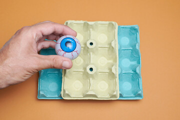 Blue eye in an egg carton with orange background