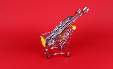 Metal wrenches of different sizes in miniature metal shopping trolley on red background