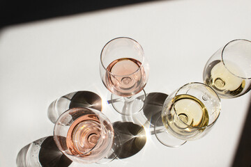 White and rose wines into glass on white table with black shadow above view