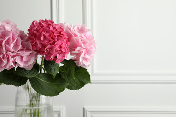 Vase with beautiful hortensia flowers near white wall. Space for text