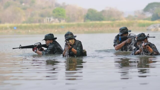 Group of soldier appear from water in canal or river and point gun around to guard from enemy during war.