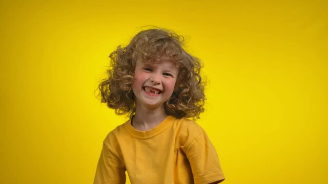 Cute curly girl with a charming toothless smile is smiling in a yellow studio