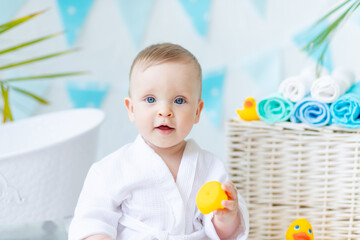 portrait of a baby boy sitting after bathing in the bath in a white robe with a rubber duck and a...