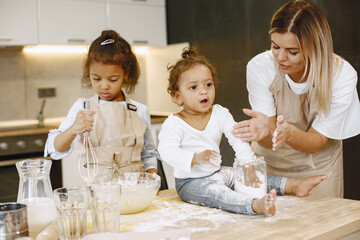 Two children in a kitchen with their mother. Little girls with a dough. Kid in a beige apron