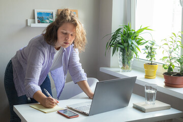 woman working at home with laptop and white table notebook pen and phone stand and write