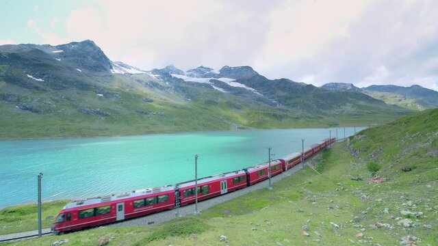 Red train of the Alps passes near a lake near the Bernina Pass