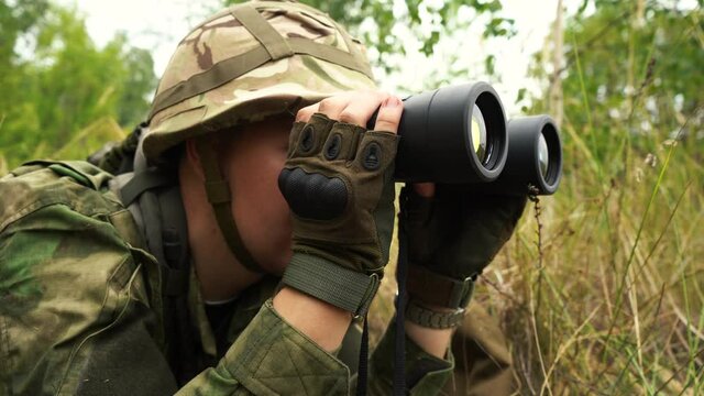 soldier looking through binoculars lying in the bushes