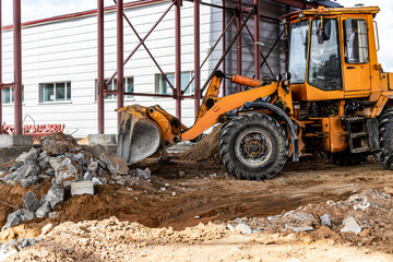Fototapeta na wymiar A front-end loader at a construction site removes debris from reinforced concrete. Collection and removal of detached building materials.