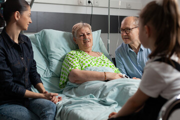 Sick retired grandmother talking with grandchild while resting in bed after medical surgery in hospital ward. Family visiting grandparent supporting during illness examination. Healthcare therapy