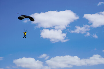 
a man glides with a parachute against the background of a blue sky with white clouds, a parachutist