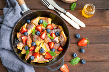 Kaiserschmarrn - traditional austrian pancake dessert with fresh berries and powdered sugar on a dark wooden background. Sweet breakfast. Copy space.