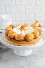 Saint Honore cake with profitrols, caramel, custard and whipped cream on a white plate on a gray concrete background. Traditional French dessert. Copy space.