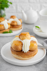 Saint Honore cake with profitrols, caramel, custard and whipped cream on a white plate on a gray concrete background. Traditional French dessert. Copy space.