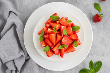 No baked cheesecake with fresh strawberries and mint on top on a white plate on a gray concrete background. Copy space.