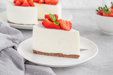 No baked cheesecake with fresh strawberries and mint on top on a white plate on a gray concrete background. Copy space.